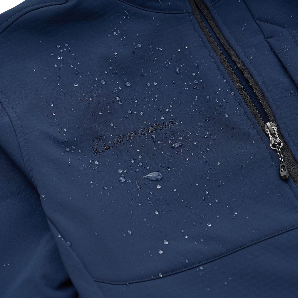Close-up of the BOEING Men's Softshell Jacket in navy blue, showing a zippered pocket and Boeing logo. Water droplets accent its 4-way stretch, water-resistant fabric.