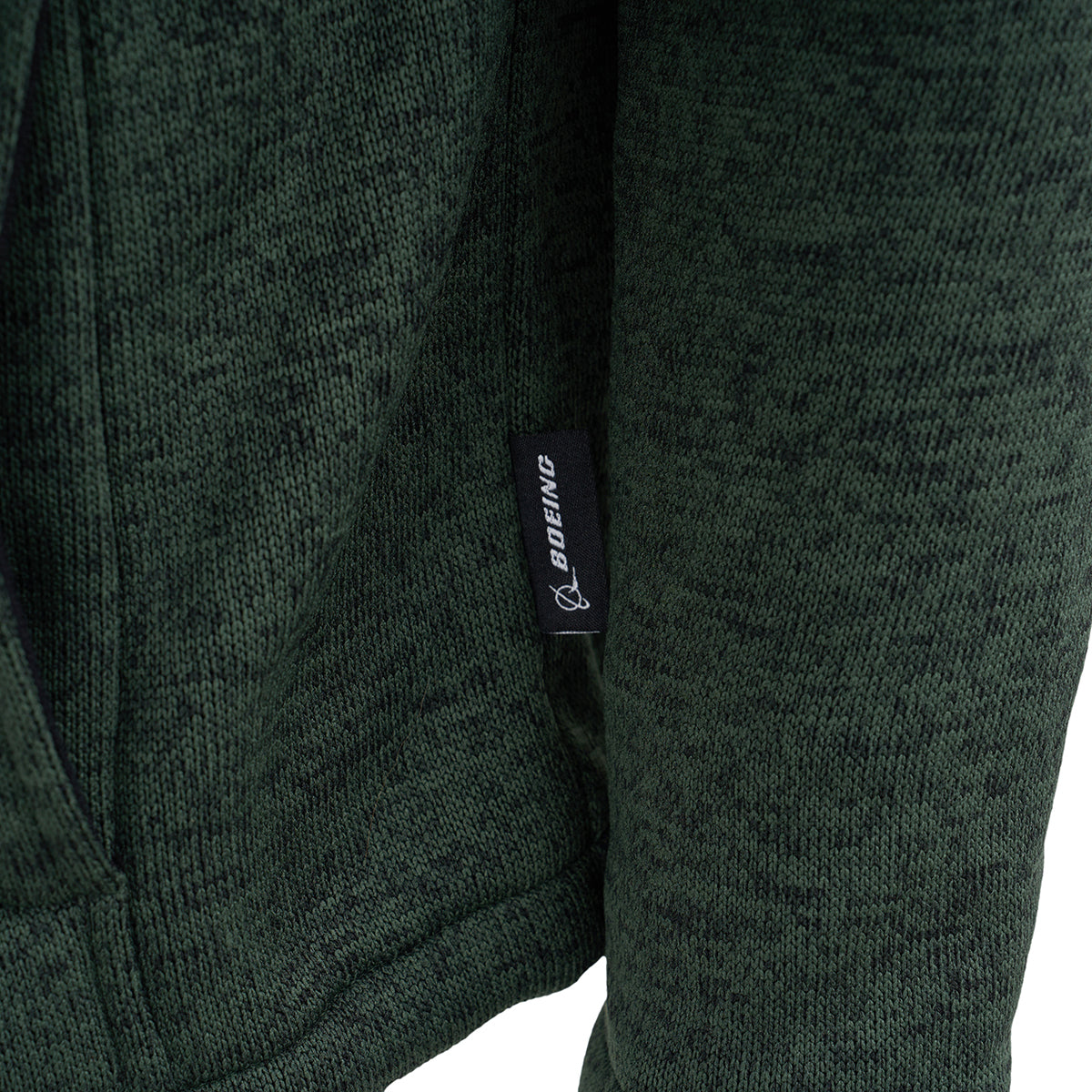 A close-up of the Boeing Men's Full-Zip Fleece Sweater, made from dark green textured fabric with cozy Sherpa lining, and a small black tag featuring the BOEING logo and text on the side seam.