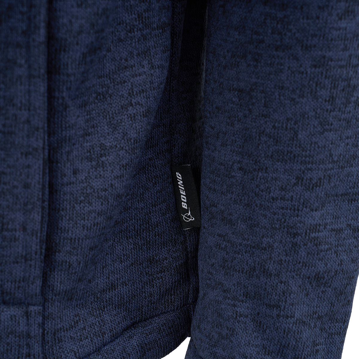Close-up of the Boeing Men's Full-Zip Fleece Sweater by BOEING, featuring textured dark blue fleece and a small black tag with the Boeing logo stitched into the seam.