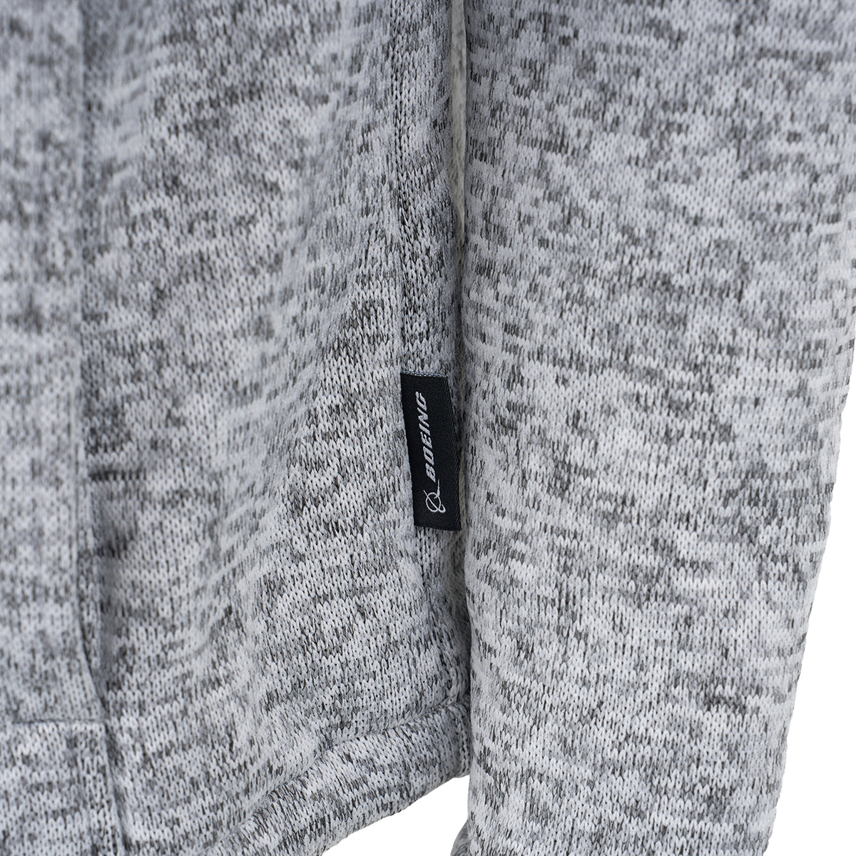 Close-up of a gray and white speckled Boeing Men's Full-Zip Fleece Sweater with a small black tag featuring white BOEING branding, attached to a seam.