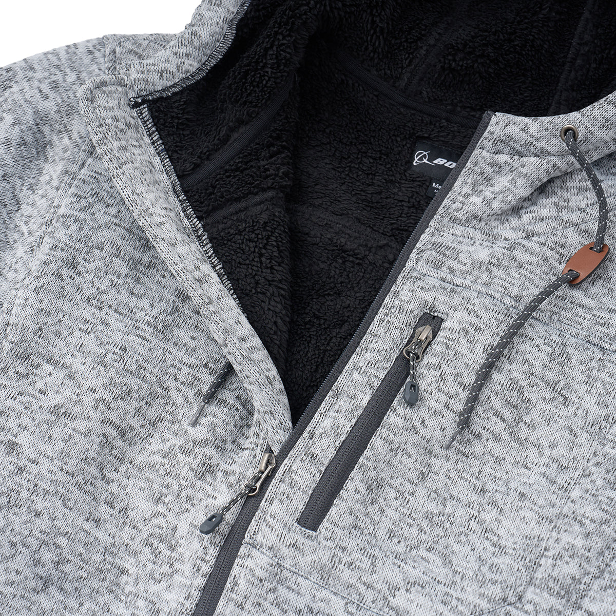 Close-up of the Boeing Men's Full-Zip Fleece Sweater by BOEING, featuring a gray fleece exterior, soft black Sherpa lining, zippered chest pocket, drawstring hood, and a small leather accent on the string.