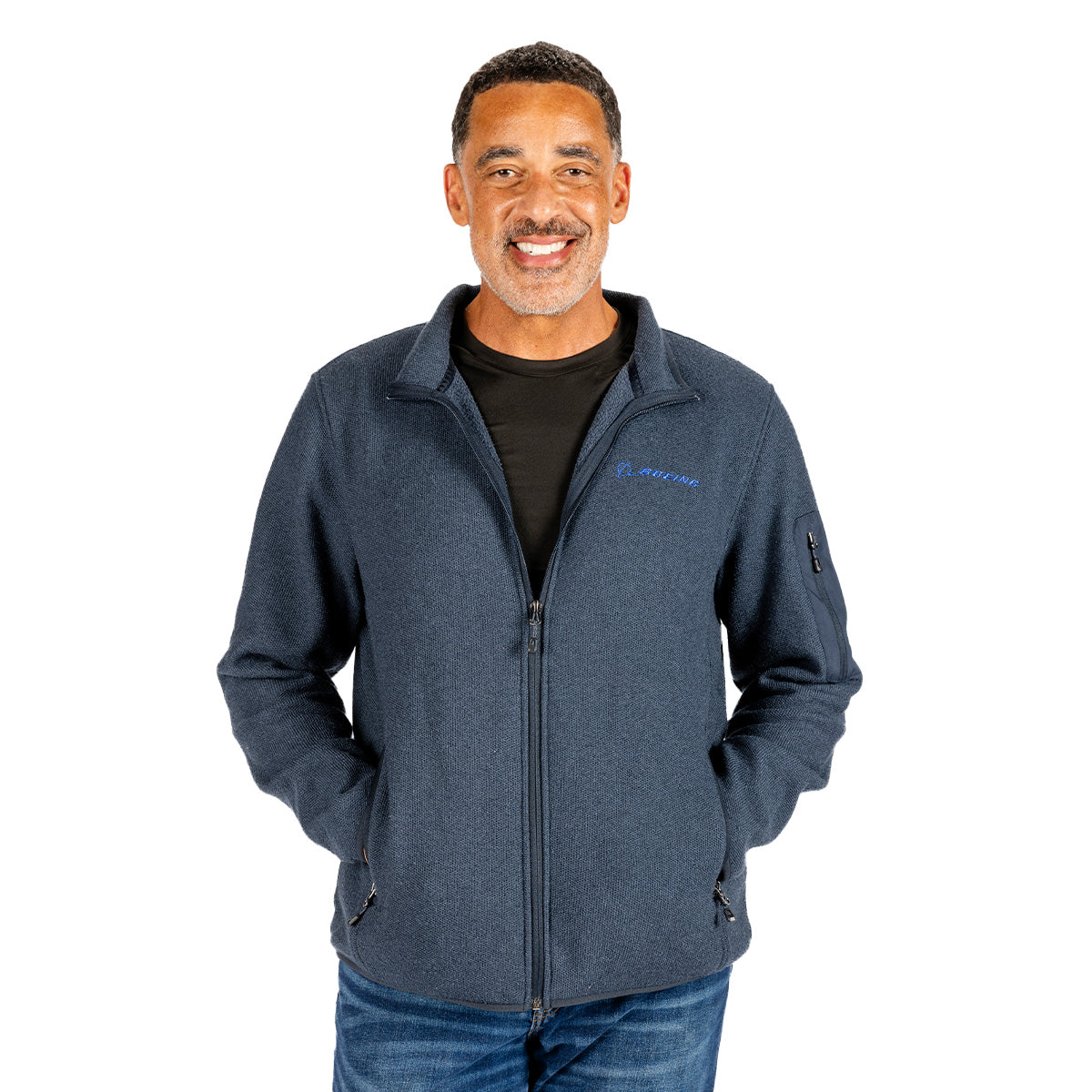 A smiling man wears a navy blue Boeing Unisex Full-Zip Pique Fleece featuring a Boeing logo and a zippered sleeve pocket.