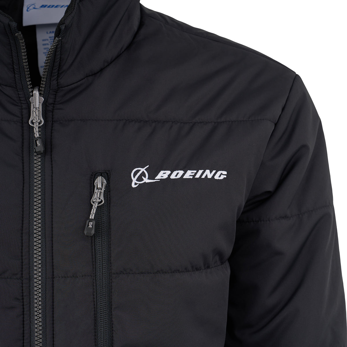 Close-up of the Boeing Men's 3-in-1 Systems Jacket by BOEING in black, showing a white embroidered Boeing logo on the chest, a zippered chest pocket, and part of the main zipper.