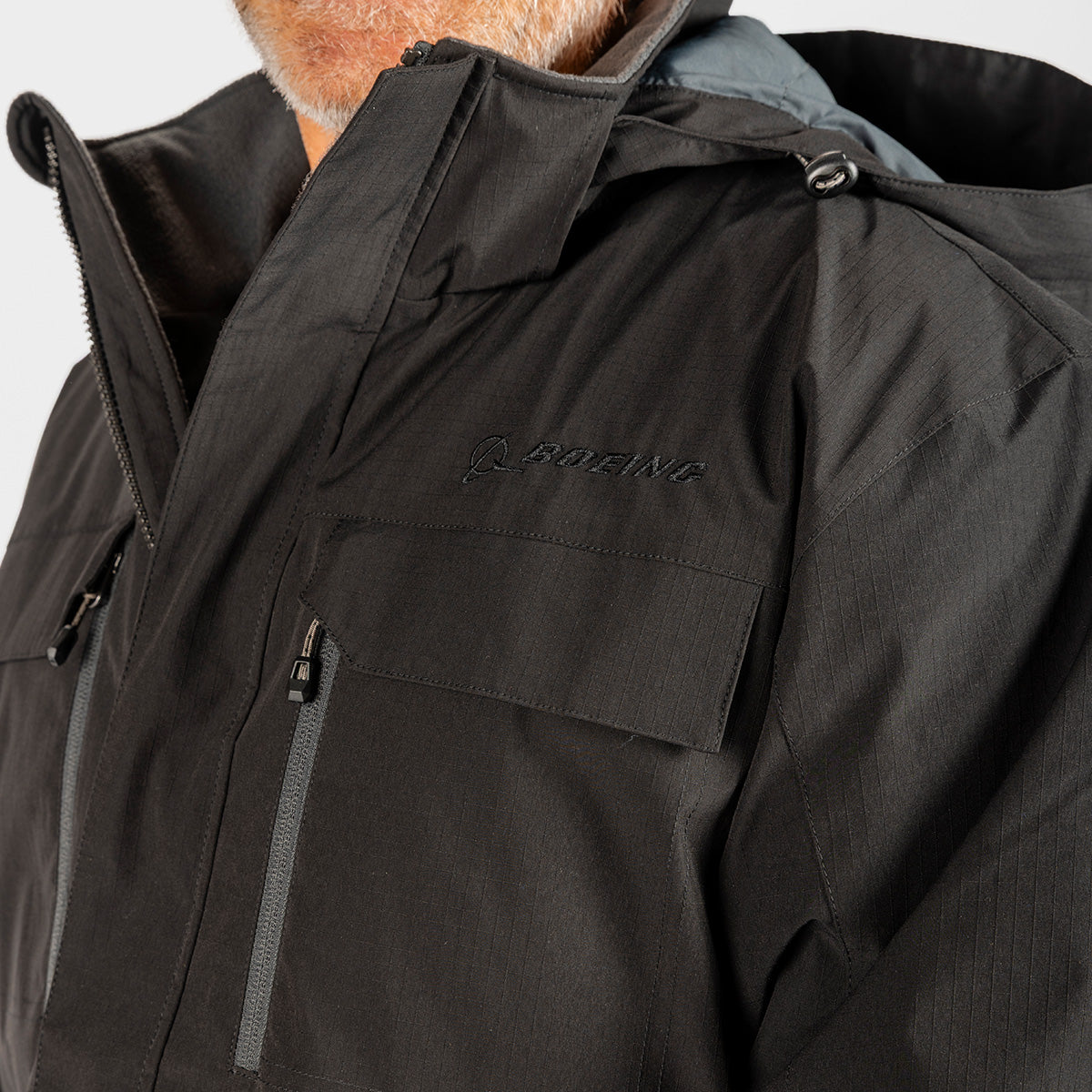 Close-up of a black hooded Boeing Men’s Workman Jacket featuring a zippered chest pocket and the BOEING logo embroidered on the upper chest.