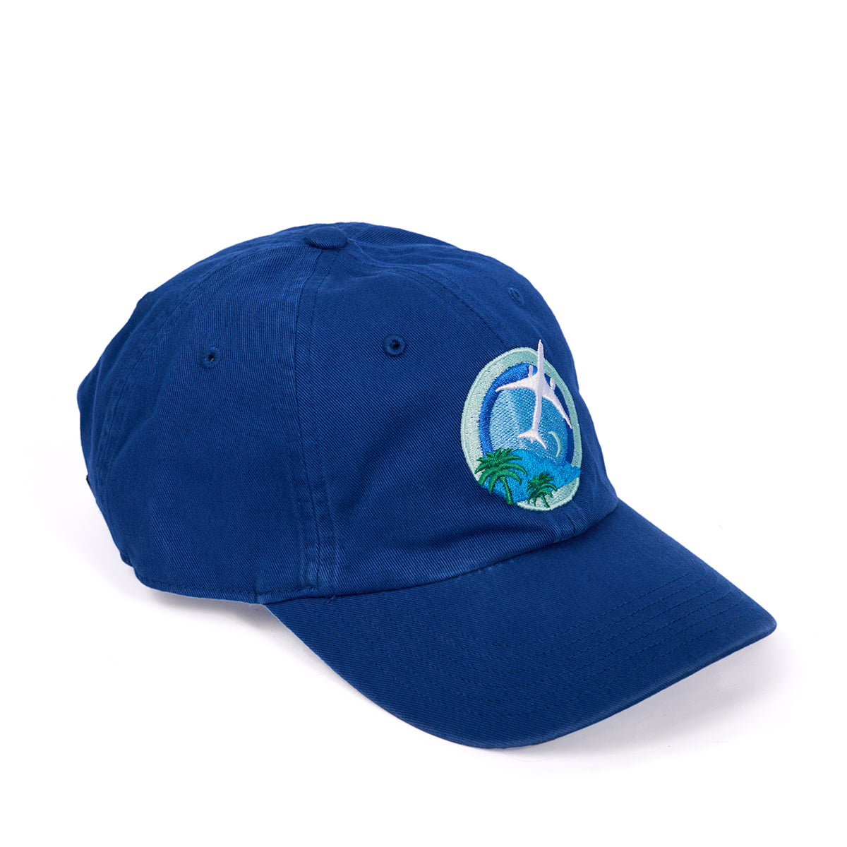 The Boeing 787 Dreamliner Skyward Hat, by Boeing, is a blue baseball cap with a curved brim. It features an embroidered white airplane flying over a green palm tree against a blue sky and includes an adjustable cloth backstrap for the perfect fit.