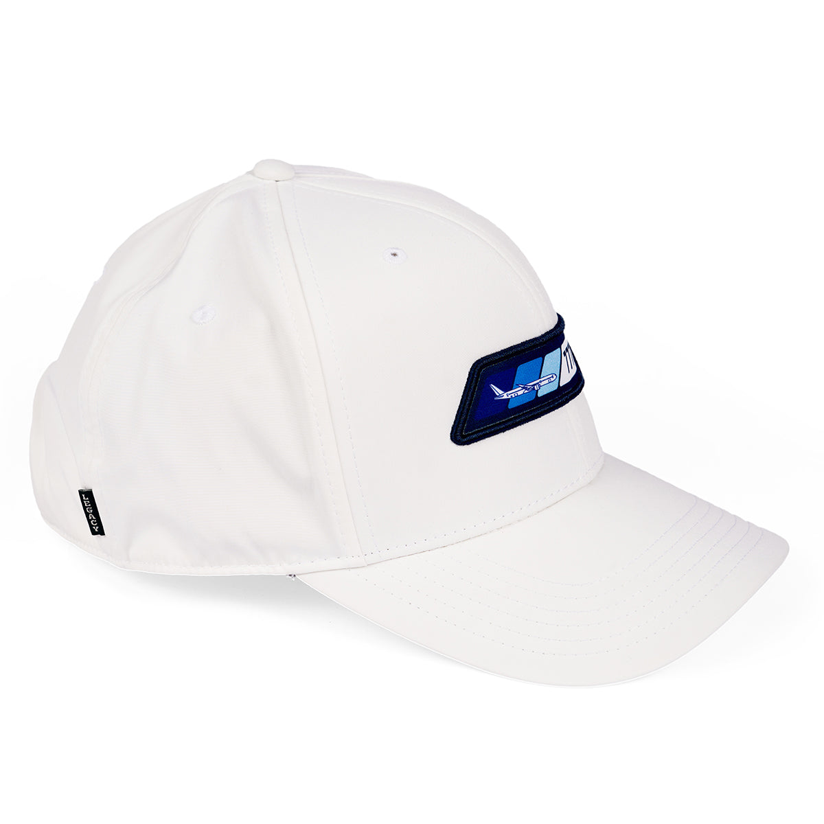 The Boeing 777X Velocity Unisex Hat is a white baseball cap with a blue rectangular patch of geometric shapes, moisture-wicking fabric, visible stitching, and an adjustable Velcro closure. Featuring a small black side tag, it stands out against a plain white background.