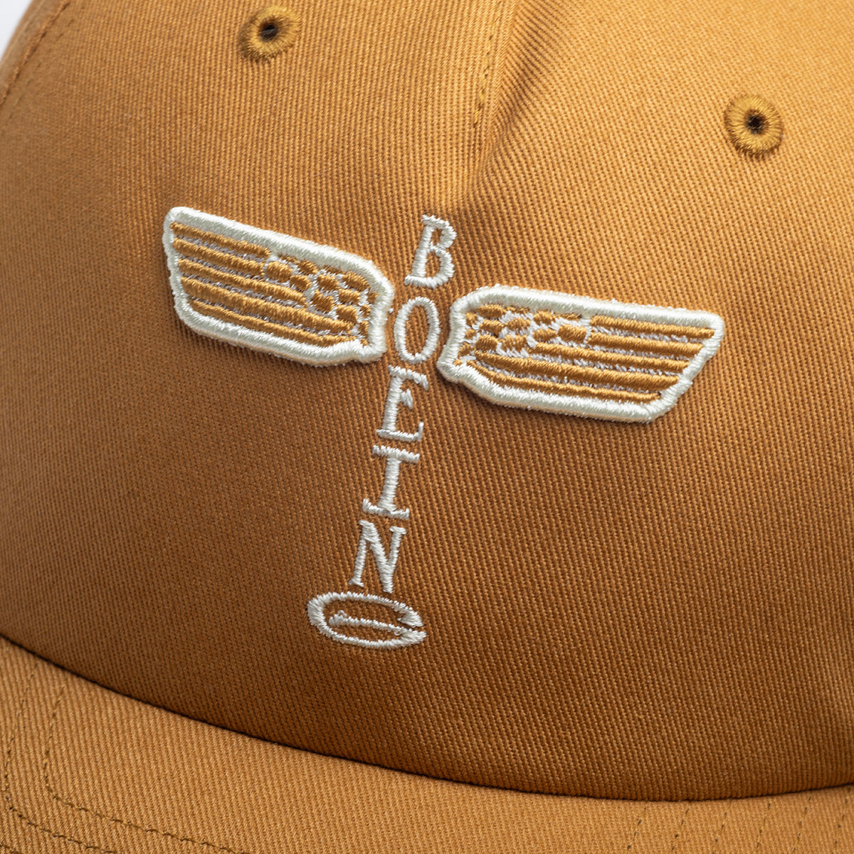 A close-up of the Richardson Boeing Airplane Logo Snapback Hat in tan, featuring an embroidered vintage BOEING winged logo in white thread.