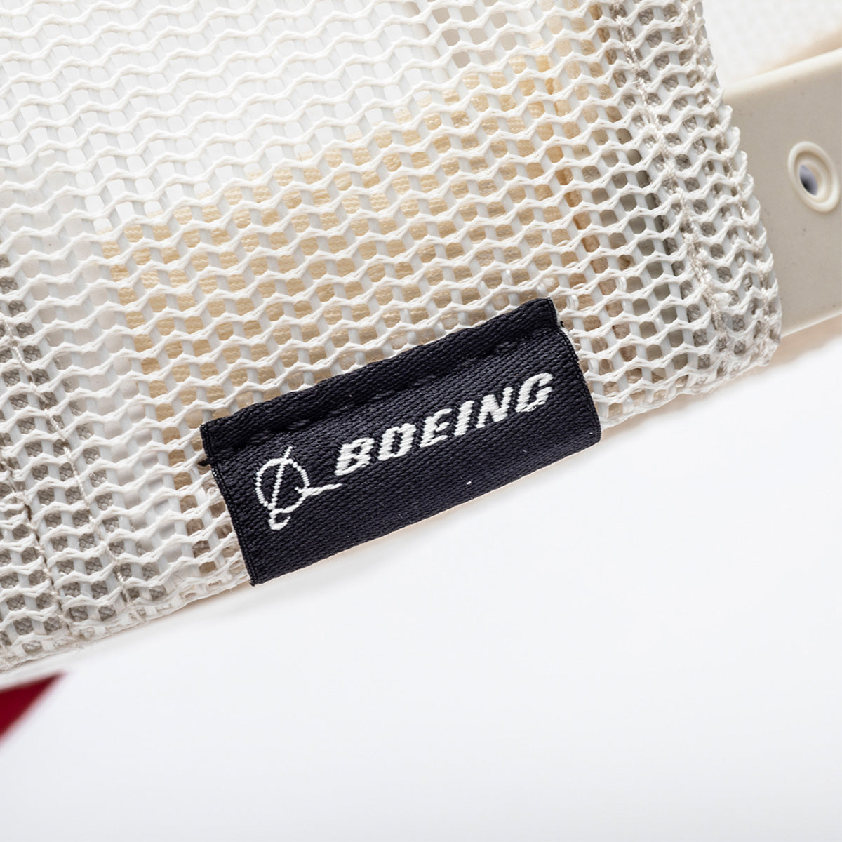 A close-up of white mesh fabric with metal grommets and a black tag showing the BOEING logo—ideal for the Richardson Boeing Script Logo Trucker Hat by BOEING.