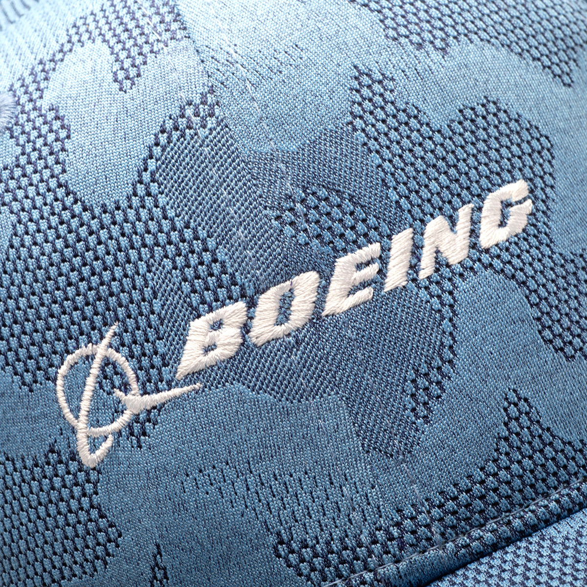 Close-up of the Boeing Signature Logo Camo Hat—a blue camo snapback with white embroidered BOEING lettering and signature logo above the brim. Adjustable closure ensures a comfortable fit.