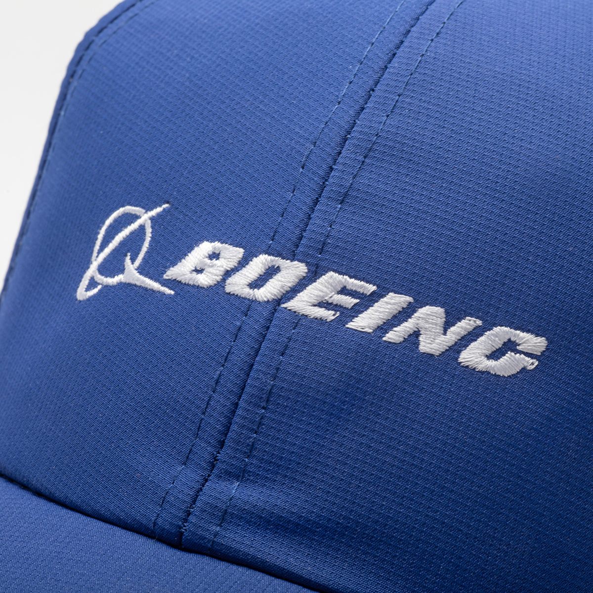Close-up of the Boeing Signature Logo Performance Hat by BOEING, a blue moisture-wicking snapback with a white embroidered logo and swoosh on the front panel.