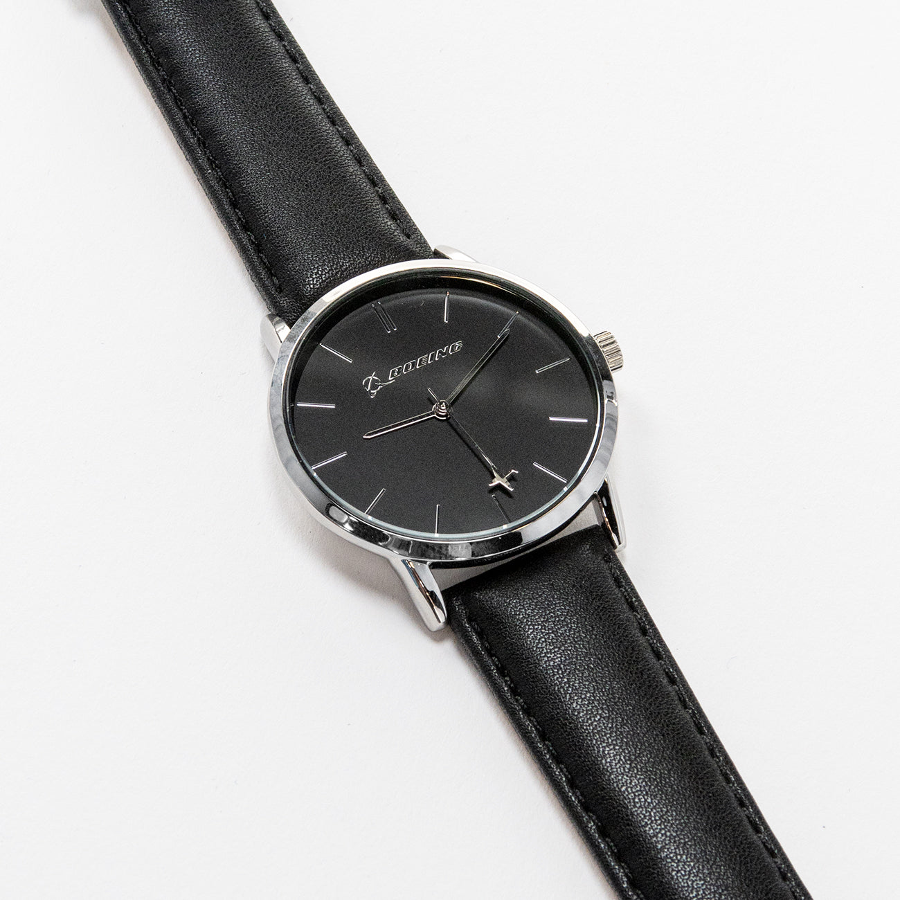 The Boeing Silver Rotating Airplane Watch by Boeing features a minimalist black dial encased in a silver case with a sleek black leather strap. Silver hour markers and hands move elegantly, showcasing timeless style as it rests gracefully on a white surface.