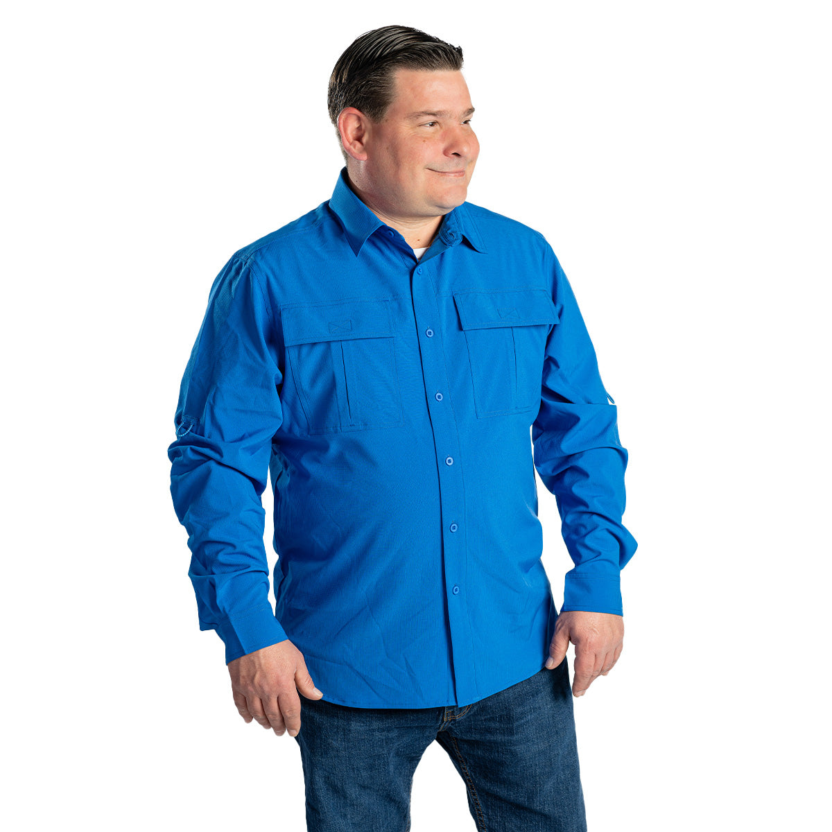 A man wears a BOEING Signature Logo Men's Long Sleeve Utility Shirt in bright blue with UPF 50+, paired with blue jeans. He stands slightly sideways against a plain white background, smiling gently with neatly combed hair.
