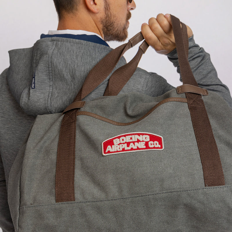 Person holding a gray bag with heritage 'Boeing Airplane Co.' logo against a light grey background