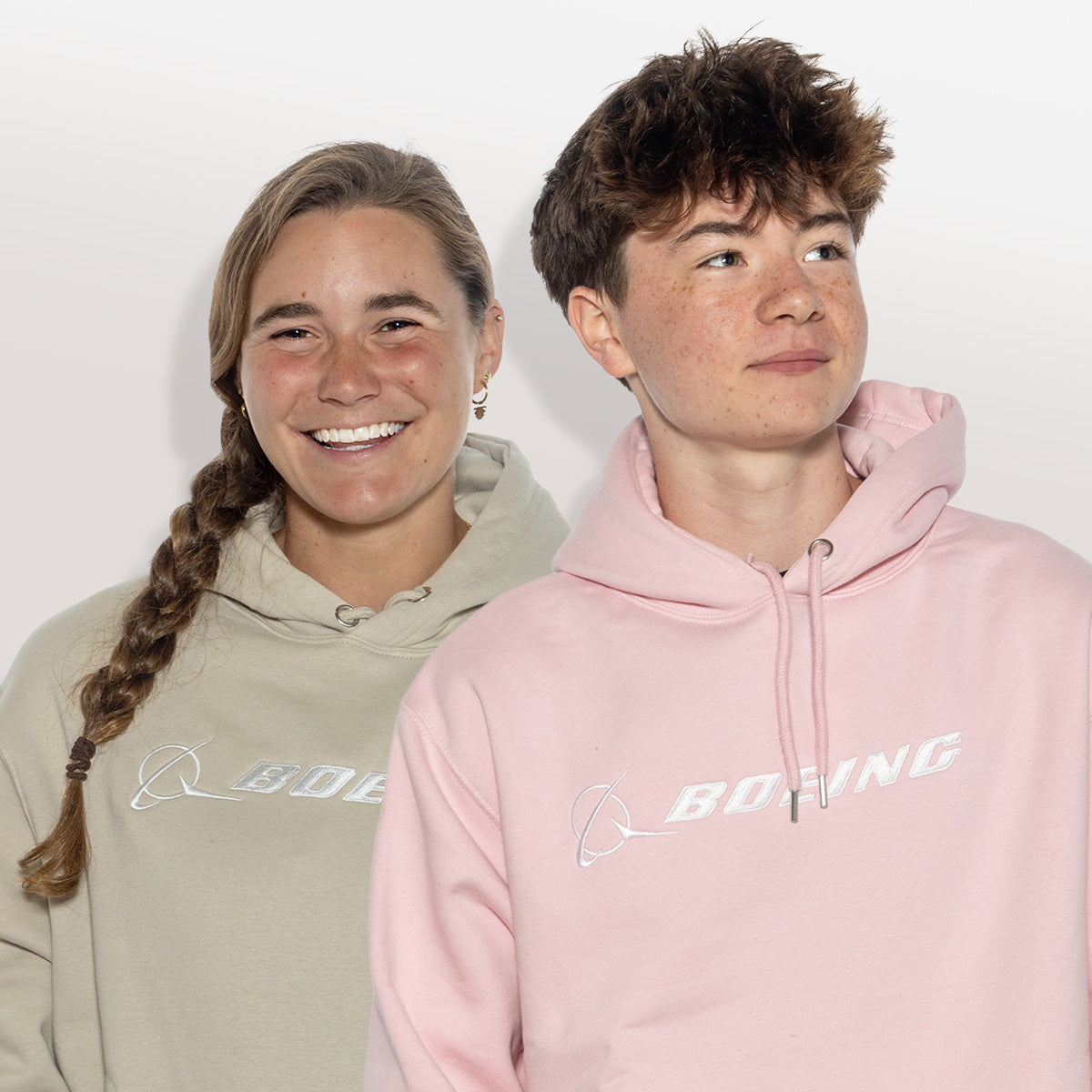Two individuals wearing hoodies, one in beige and the other in pink, both displaying the Boeing Signature logo.
