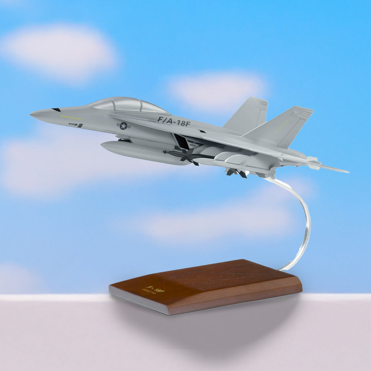 A detailed model of a F/A-18F Super Hornet jet, displayed on a wooden base with a blue sky background.