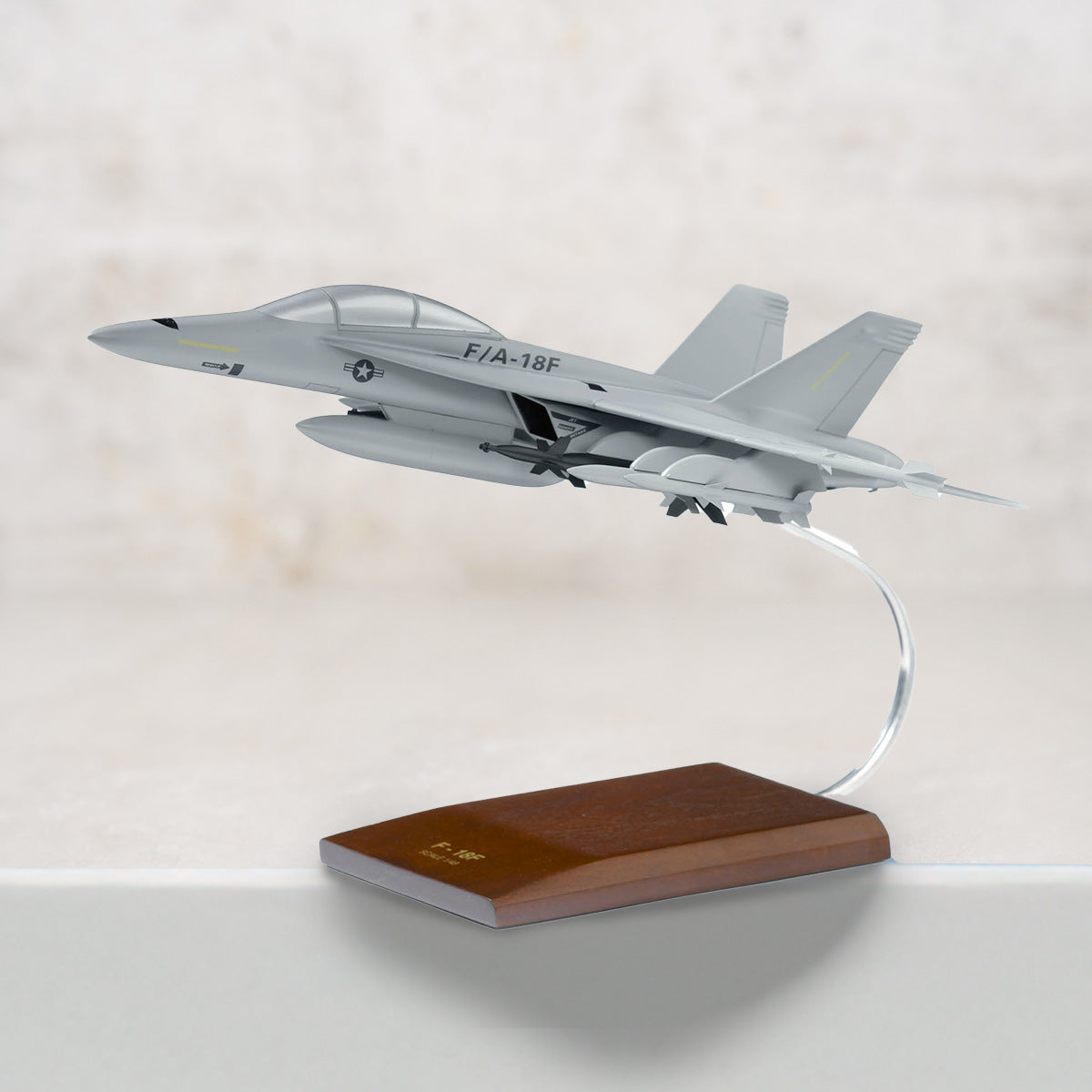 Model of an F/A-18F aircraft on a wooden base with a light gray background