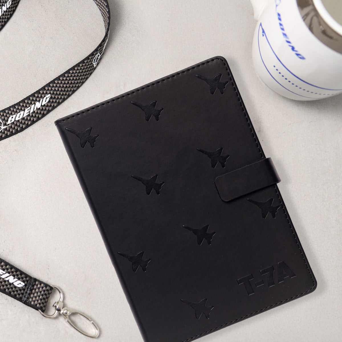 Boeing T-7A notebook, Boeing engine mug and black lanyard on a grey countertop.