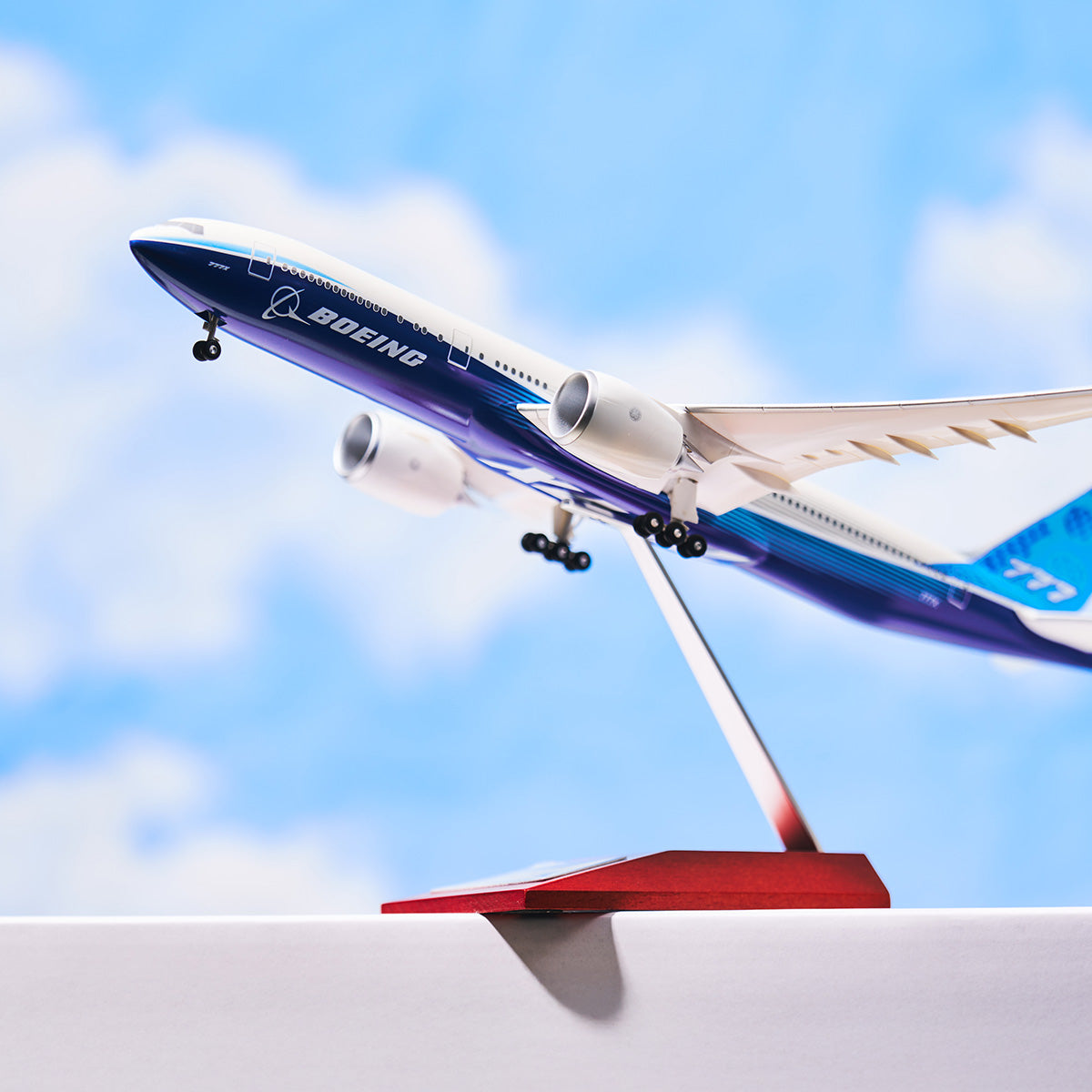 A model airplane of a Boeing 777X displayed on a stand against a blue sky background.