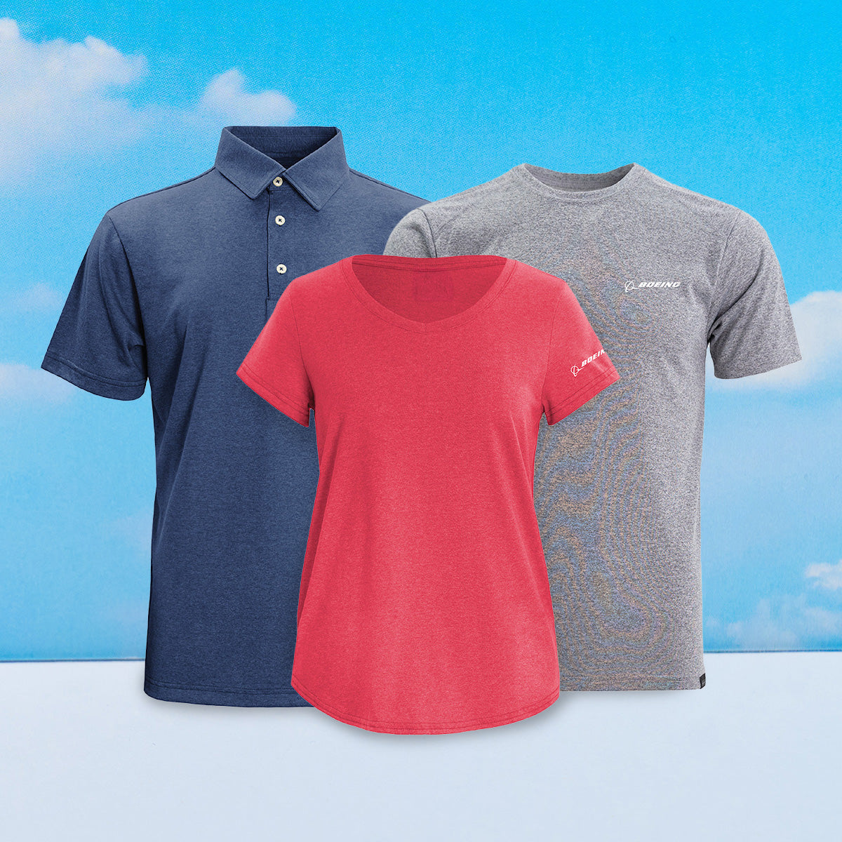 A collection of three Boeing Signature shirts: a navy polo, a red t-shirt, and a gray t-shirt, displayed against a blue sky background.