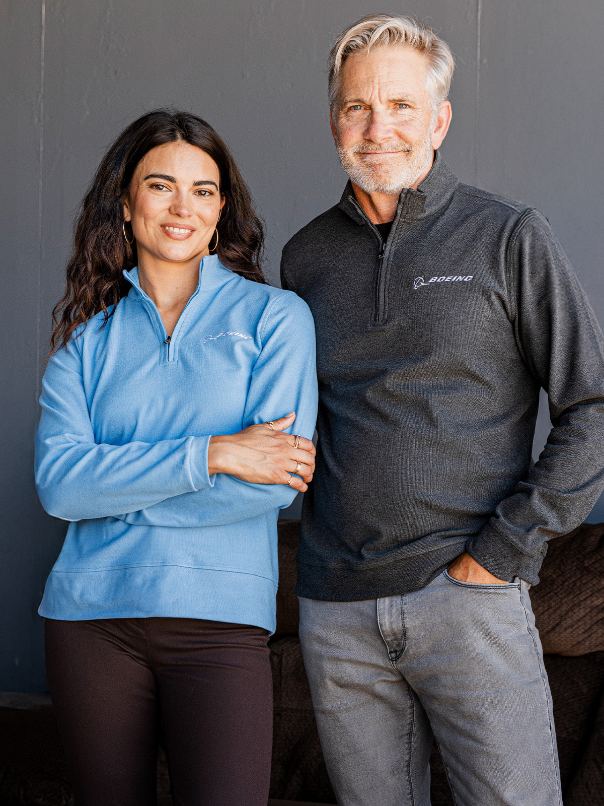 A man and a woman standing side by side wearing quarter-zip fleece pullovers with Boeing logo The woman wears a light blue pullover, and the man wears a dark gray pullover.