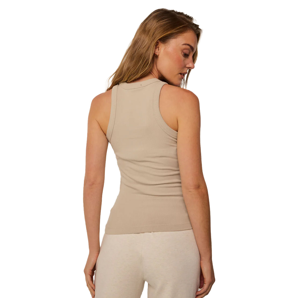 A woman with light brown hair faces away, highlighting the BOEING Greyson Boeing Womens Orion Tank Top in beige, styled with cream pants against a white background.