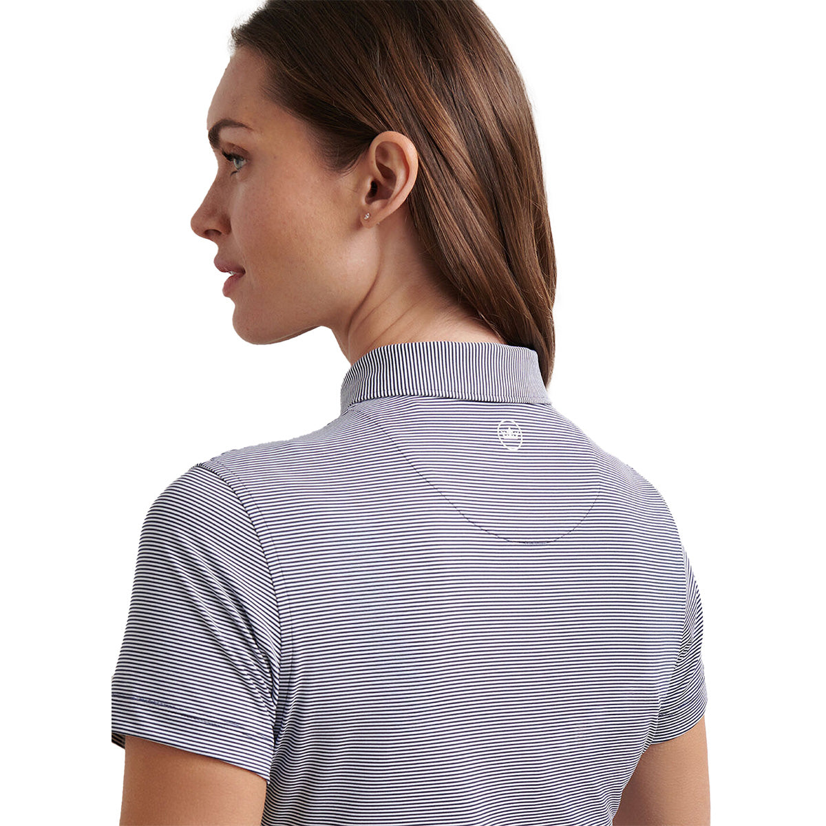 A woman with light skin and brown hair pulled back looks to the side, wearing the Peter Millar Boeing Women’s Jubilee Polo from BOEING, featuring stretch fabric with thin horizontal stripes and a small white logo on the back. Plain white background.
