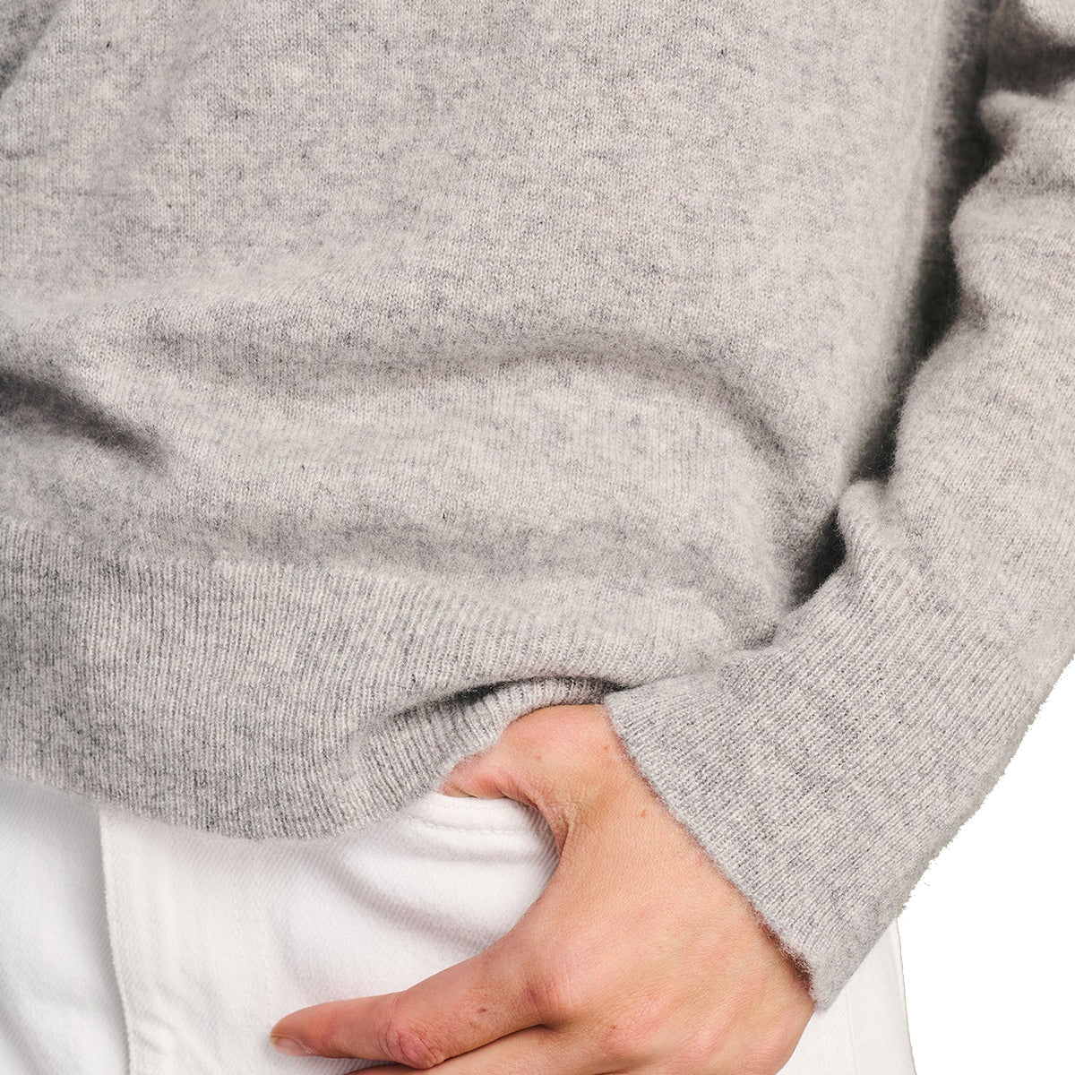 A person wearing a light gray BOEING Signature Women’s Cashmere Sweater and white pants has their right hand in their pocket.
