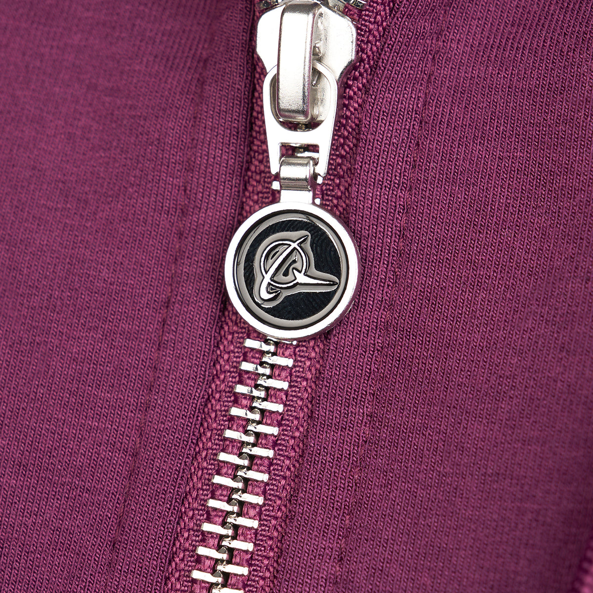 Close-up of the zipper on a Boeing Signature Logo Womens Short Waist Hoodie in purple from The Boeing Store. It features a round, metallic pull with the Boeing logo, seamlessly interlocking teeth along the fabric, and thumbholes for extra functionality.
