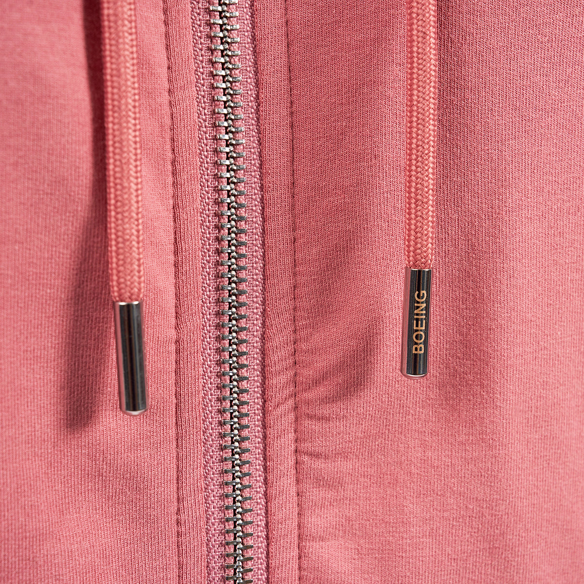 Close-up of the Boeing Signature Logo Womens Short Waist Hoodie by The Boeing Store, featuring a durable YKK zipper and sleek drawstrings with metal tips. One tip is uniquely engraved with the iconic Boeing logo.