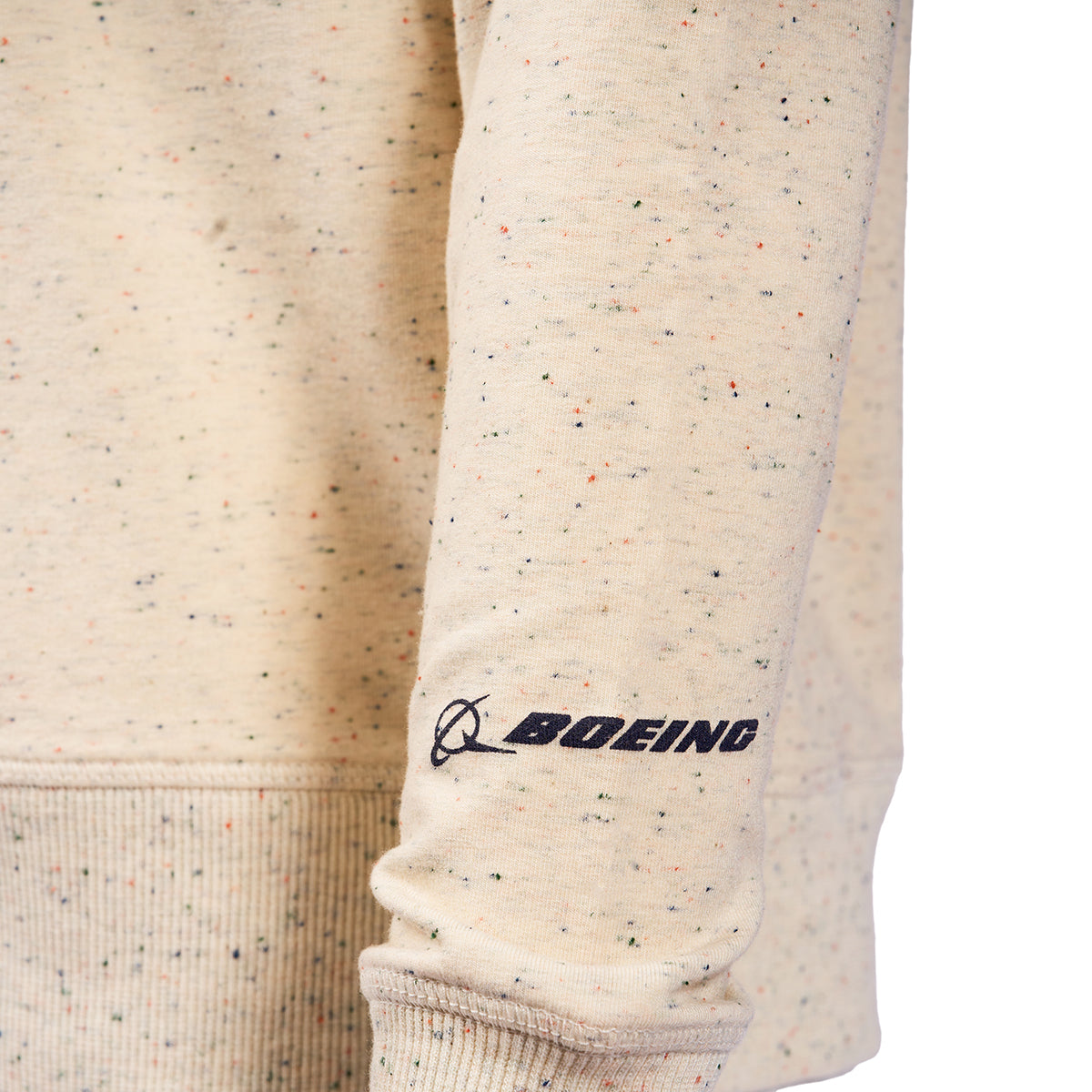 Close-up of the Boeing Women In Aerospace Womens Crewneck Sweatshirt sleeve in beige speckled design, showcasing the iconic black logo near the wrist with colorful specks adding a unique flair.