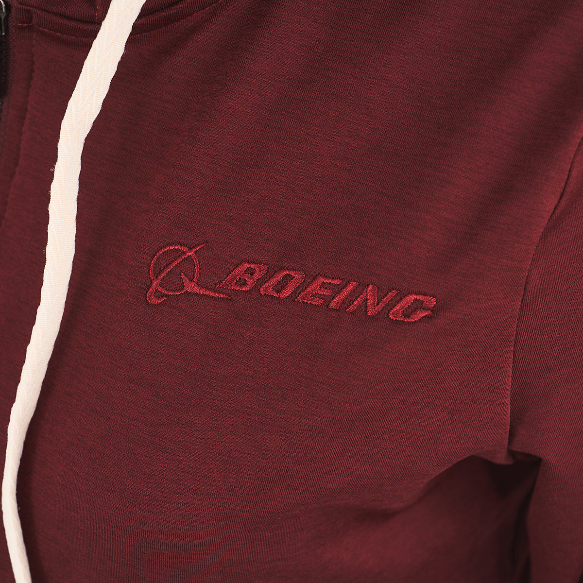 Close-up of the Glyder Boeing Women’s On-The-Go Zip-Up Hoodie, a maroon zip-up from BOEING with the logo and name embroidered in red on the chest, white drawstring accents, and part of the premium MARBLE DYE™ collection.