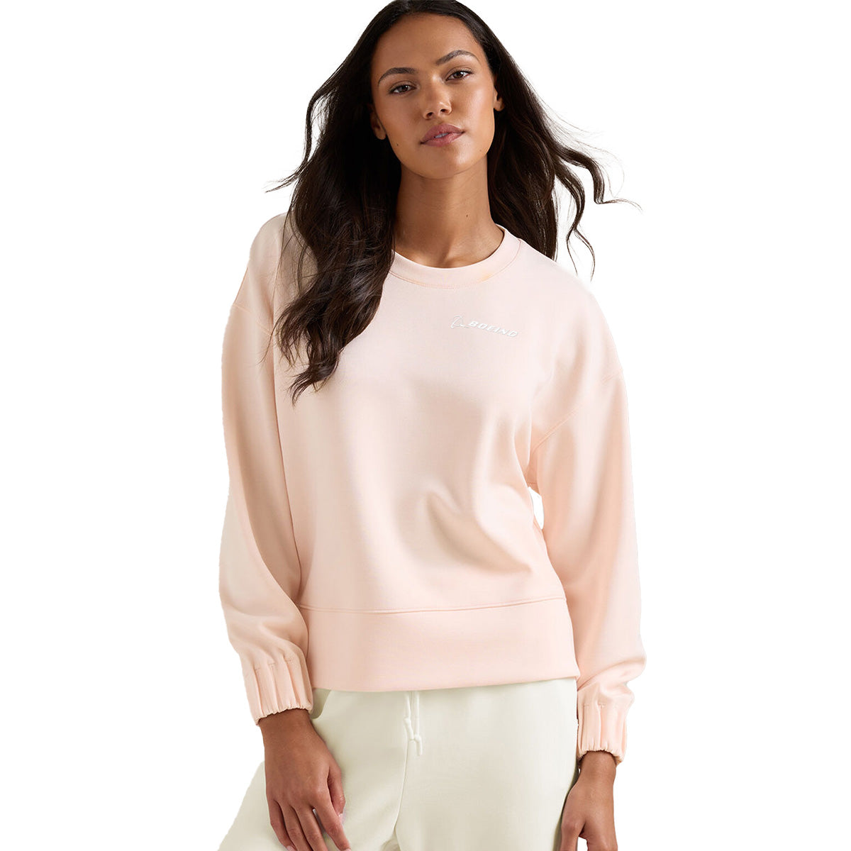 A woman models the BOEING Peter Millar Women’s Flora Knit Mélange Crewneck in light pink with long sleeves and cream pants, standing against a white background and looking confidently at the camera.
