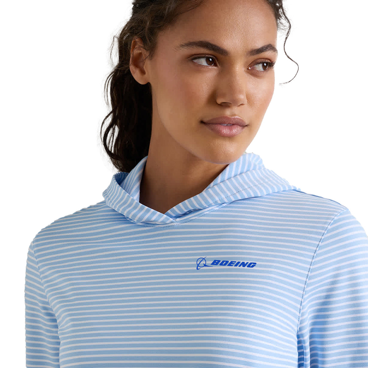 A woman stands against a plain background, looking to the side while wearing the Peter Millar Boeing Women’s Harbour Stripe Hoodie by BOEING. This hoodie features light blue and white stripes, the Boeing logo on the chest, and is crafted from moisture-wicking fabric for all-day comfort and dryness.