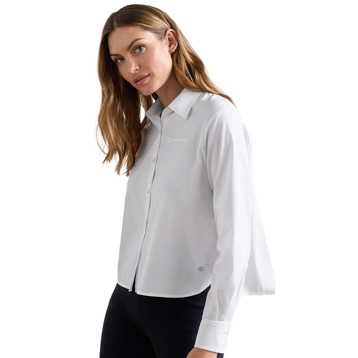 A woman with long brown hair models the Peter Millar Boeing Women’s Sylvia Button-Up Shirt by BOEING, standing slightly to the side and looking at the camera with a neutral expression against a plain white background.