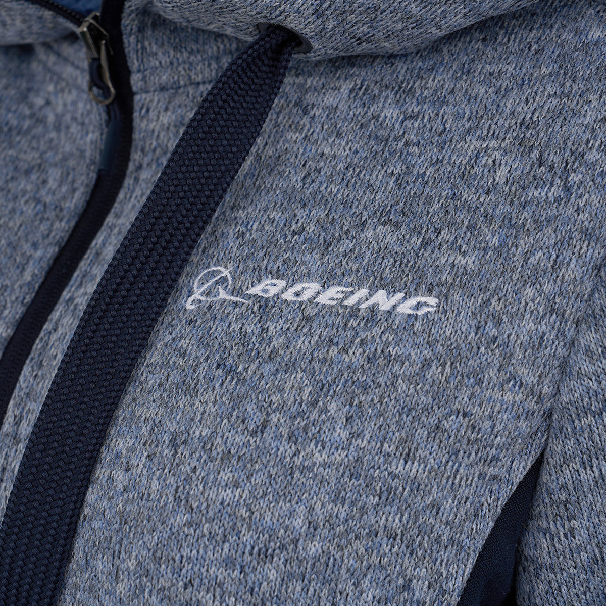Close-up of the Boeing Women's Mountain Fleece Jacket by BOEING, shown in blue and gray with black drawstrings, power stretch panels, and a white embroidered Boeing logo on the left chest.