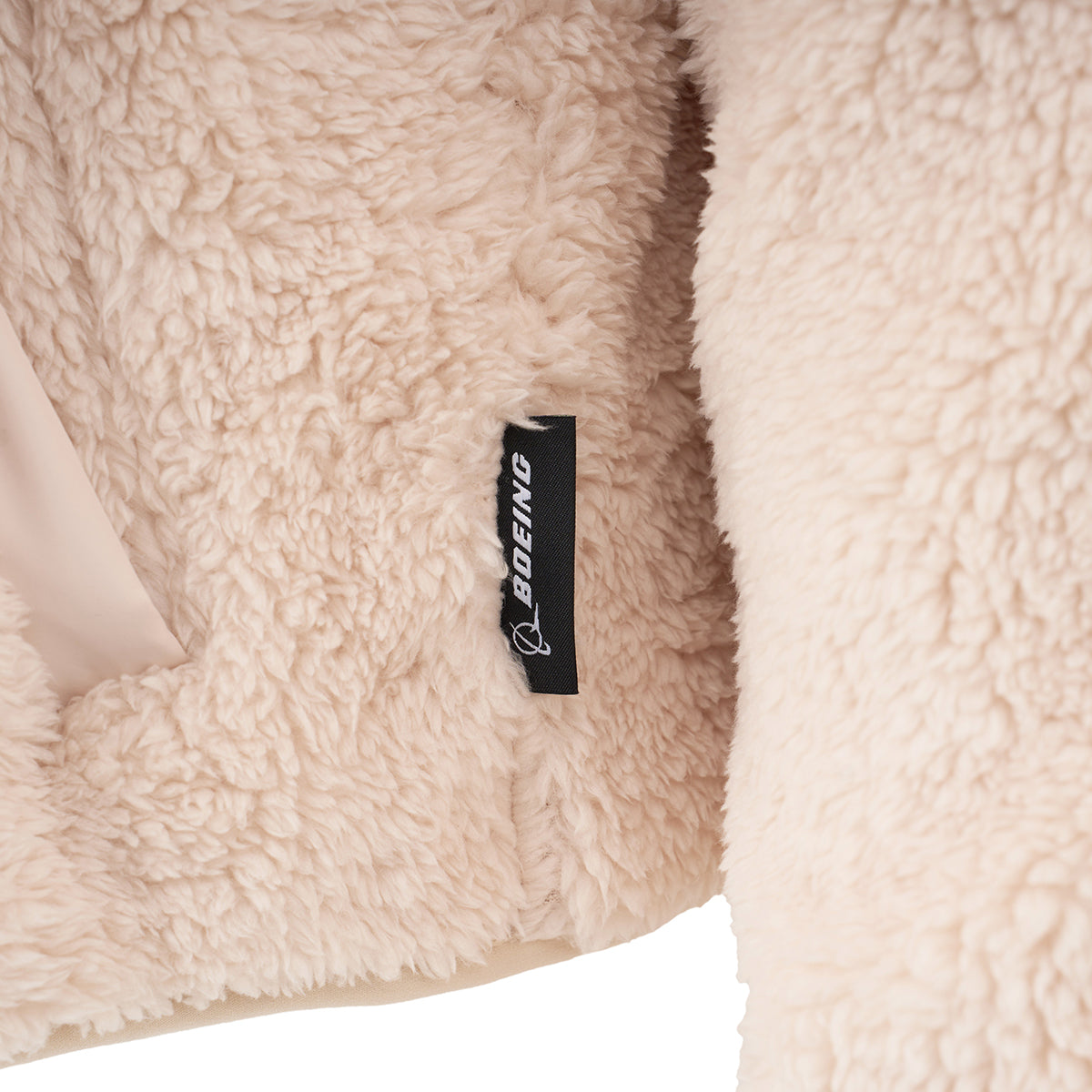 Close-up of a soft, beige Boeing Women's Sierra Sherpa Long Jacket featuring a small black tag with the white BOEING logo and text.