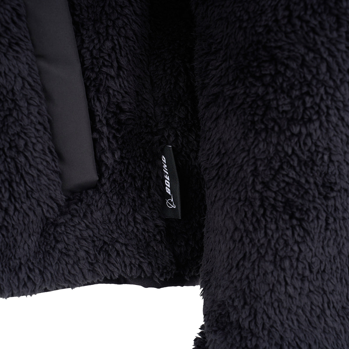 Close-up of the Boeing Women's Sierra Sherpa Long Jacket by BOEING, showing its plush sherpa fabric and a small black tag with the BOEING logo and white text.