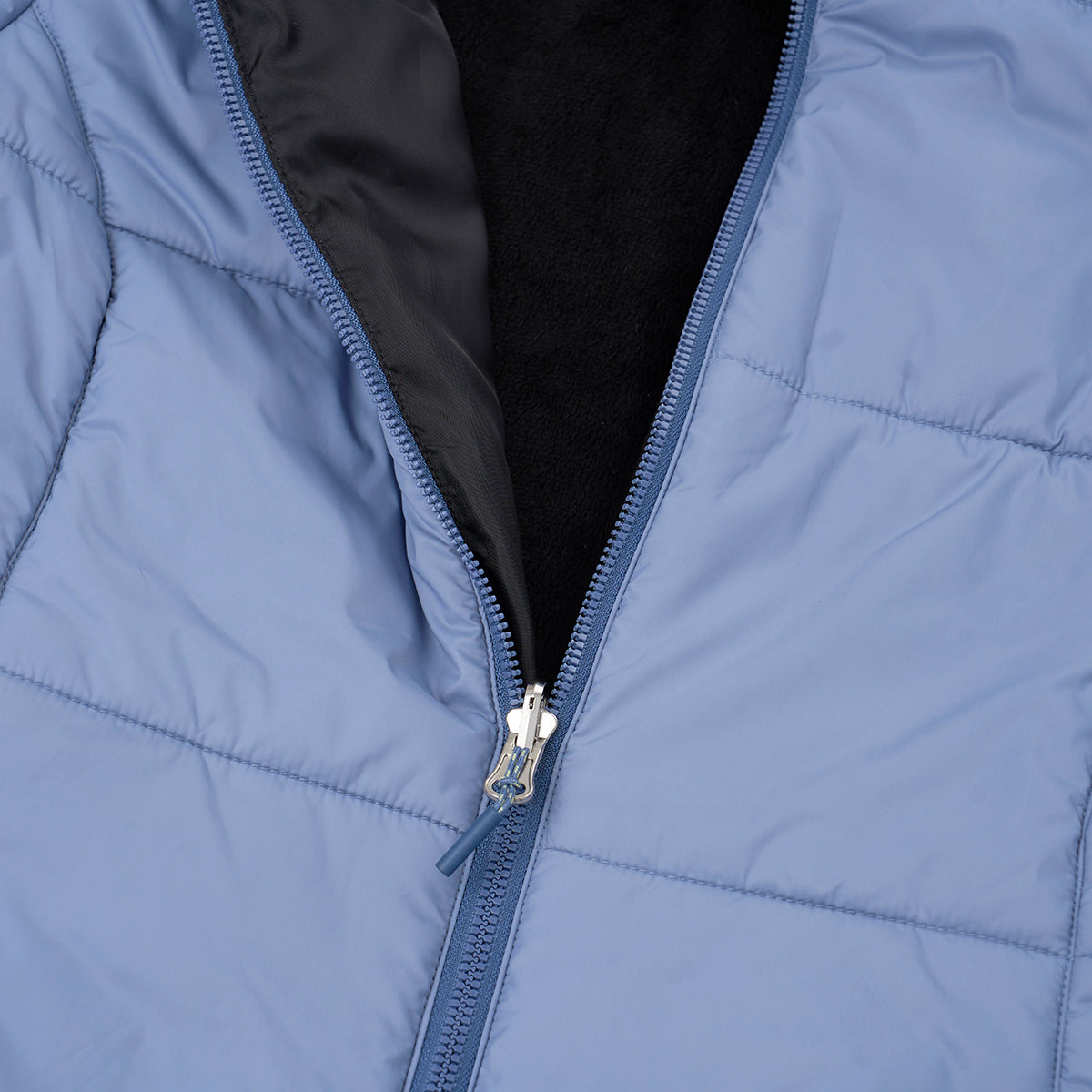 A close-up of the Boeing Women's 3-in-1 Systems Jacket by BOEING in light blue, featuring a quilted puffer design with a partially open zipper that reveals a black inner lining. This wind-resistant jacket blends comfort with modern style.