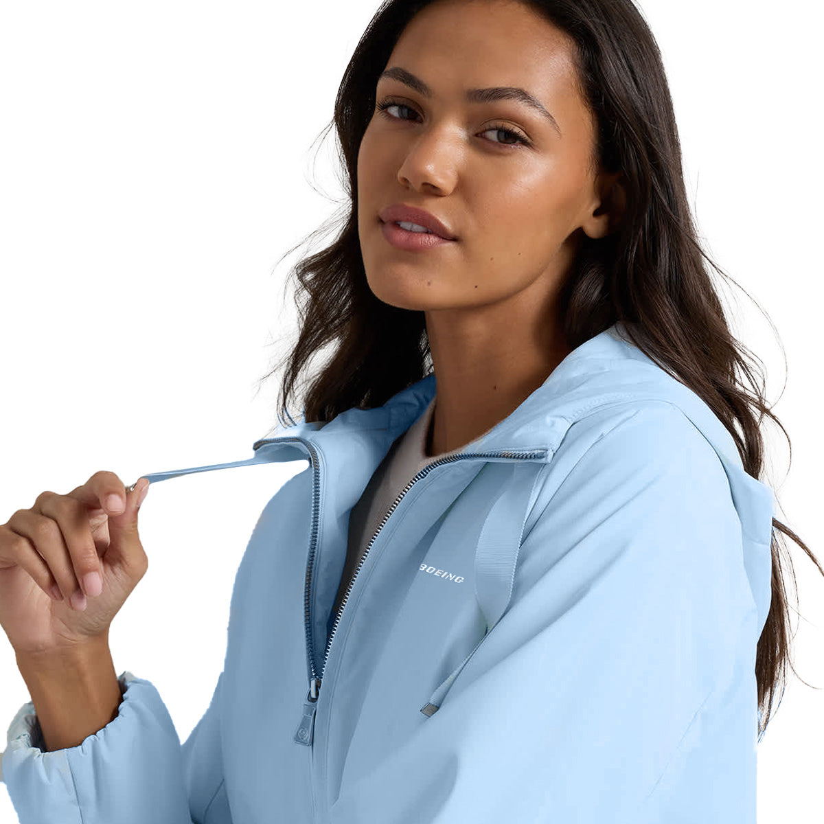 A woman wearing the Peter Millar Boeing Women’s Robinson Air Hooded Jacket in light blue stands against a white background, holding the zipper string and looking at the camera. This wind- and water-resistant jacket by BOEING features a hood and displays the Boeing logo for a stylish yet functional touch.