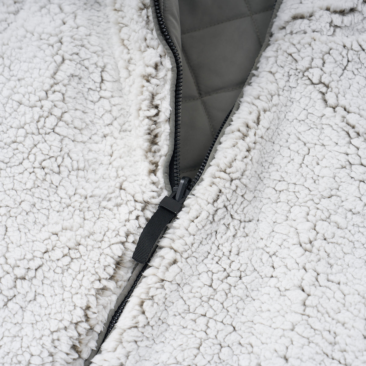 Close-up of a partially unzipped zipper on the Boeing Women's Stratus Lite Reversible Vest by BOEING, featuring fluffy white sherpa, a quilted gray lining, and wind-resistant design for comfort.