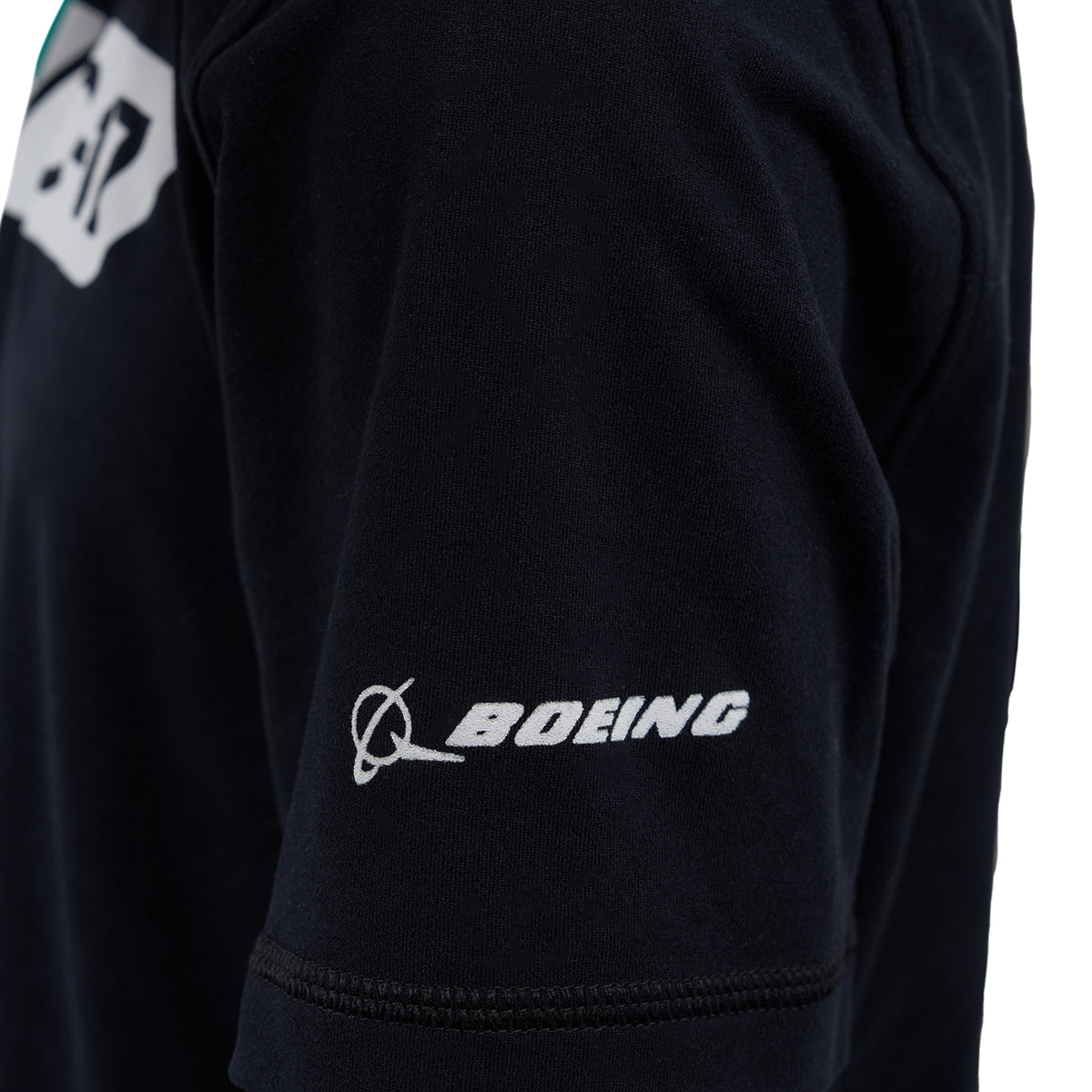 Close-up of a black Boeing C-17 Globemaster Velocity Kids’ Tech Stretch T-Shirt shows the white BOEING logo and name embroidered on the sleeve, crafted from high-performance fabric.
