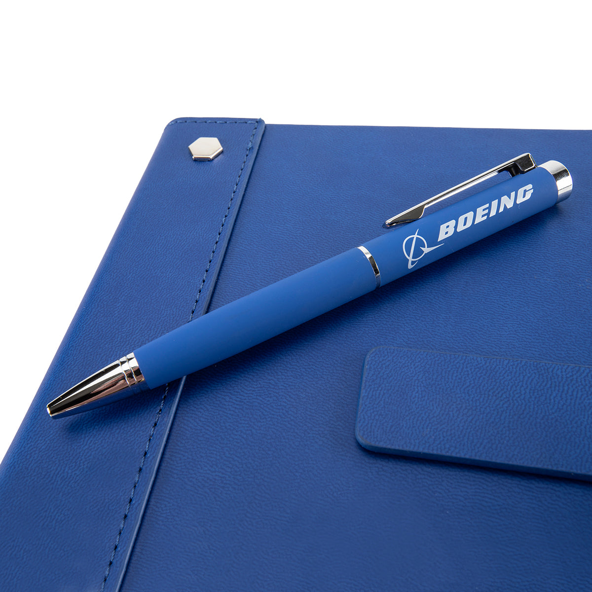 The Boeing Signature Logo Notebook Pen Set by BOEING features a blue pen with the Boeing logo, resting on a closed notebook with a soft PU leather cover and hexagonal metal detail.