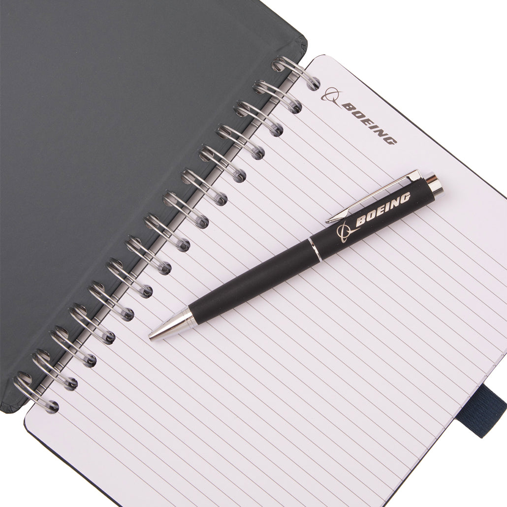A Boeing AH-64 Apache Graphic Notebook Pen Set consisting of a spiral-bound notebook with lined pages and a black retractable pen resting on top.