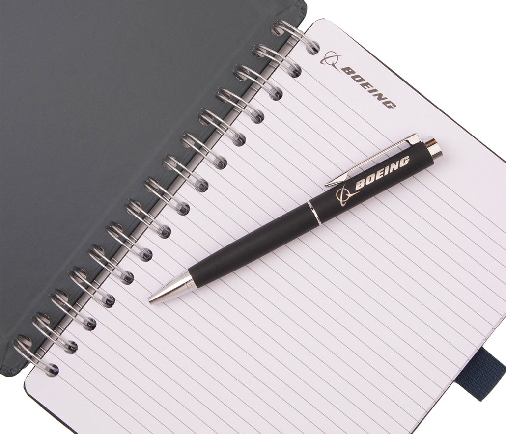 A Boeing AH-64 Apache Graphic Notebook Pen Set consisting of a spiral-bound notebook with lined pages and a black retractable pen resting on top.