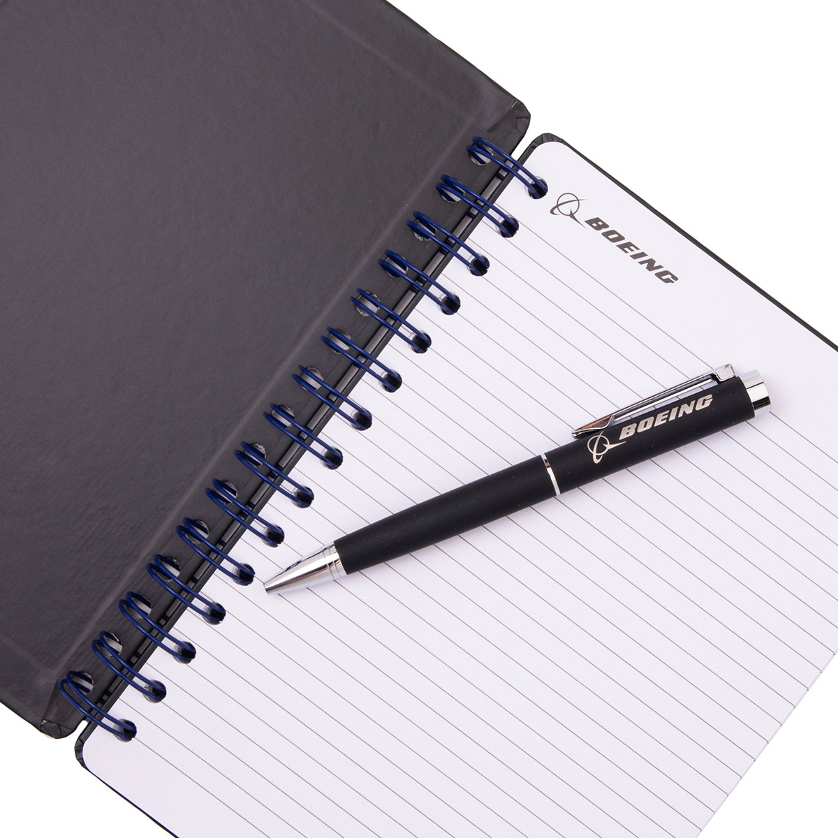 Boeing CST-100 Starliner Graphic Notebook Pen Set featuring a spiral-bound notebook with lined paper and a matching pen resting on the open page, both displaying the CST-100 Starliner logo.