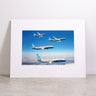 The Boeing 737 MAX Family Sky Matted Print - Small by Boeing is shown framed and matted, featuring four 737 MAX airplanes soaring against a blue sky with clouds. Displayed on a light-colored surface against a plain white wall, this high-resolution digital print delivers striking detail and clarity, and includes the iconic Boeing logo.