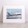 Showcased on a light surface against a plain white background, the Boeing 777-9 Matted Print - Small by Boeing features a high-resolution image of a Boeing 777 airplane soaring above the clouds. This elegant matted print delivers exceptional clarity through digital printing and proudly displays the iconic Boeing logo.