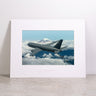 The Boeing KC-46A Pegasus Matted Print - Large by Boeing features a high-resolution digital image of a gray military aircraft soaring above clouds with a snow-capped mountain in the background, presented as a framed, matted print and displayed against a light-colored wall.