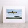 The Boeing MQ-25A & MQ-28 Matted Print - Small by Boeing features a high-resolution digital image of two military drones—one in flight and one on the ground—set against a clear blue sky. The framed print, branded with the embossed Boeing logo beneath the photograph, is displayed on a gray surface.