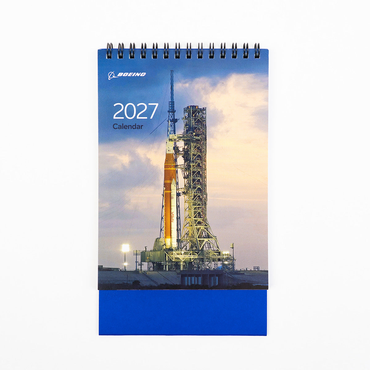 The spiral-bound Boeing 2027 Desktop Calendar from BOEING features a striking cover photo of a rocket poised on its launch pad at dusk, framed by clouds and floodlights—an image that highlights the innovative aerospace products central to BOEING’s legacy.